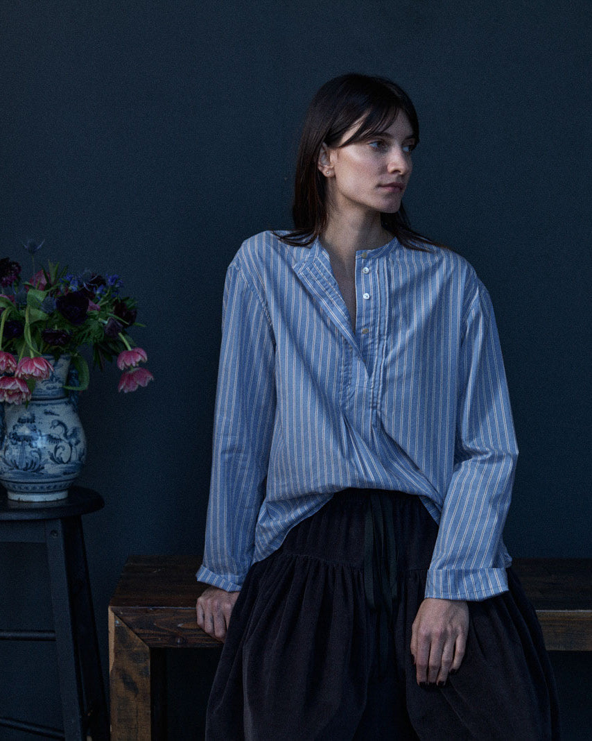 Woman wearing a blue striped shirt against a dark background with flowers on a table.