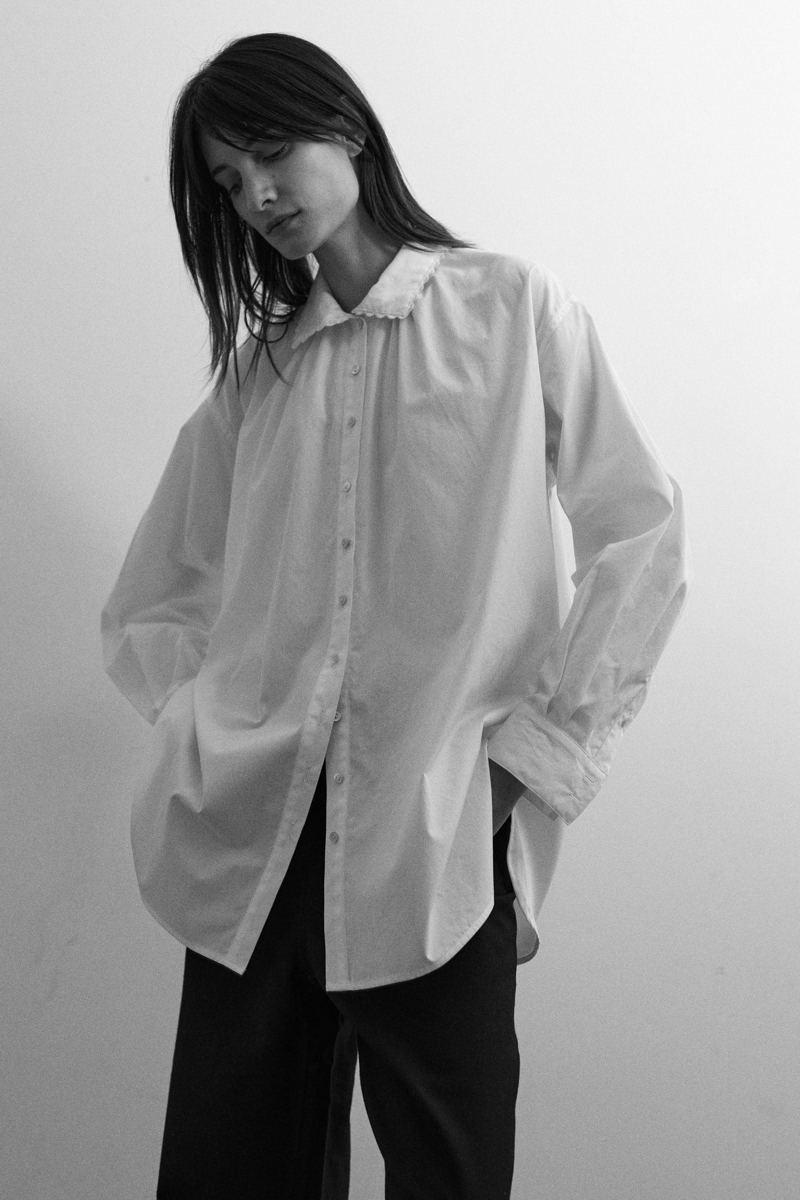 Person wearing a white oversized shirt with a high collar against a plain background