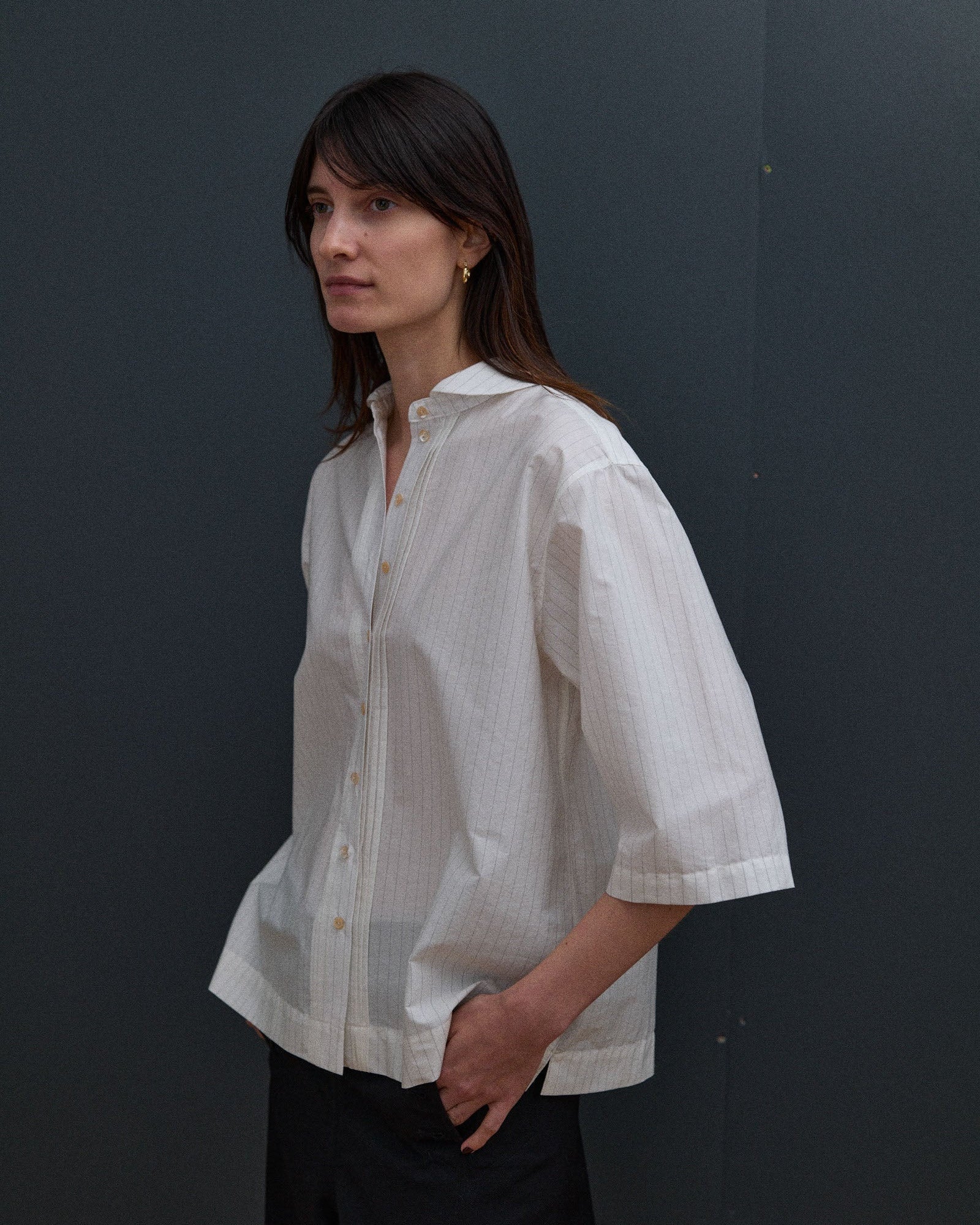 Woman wearing a white shirt with thin stripes against a dark background