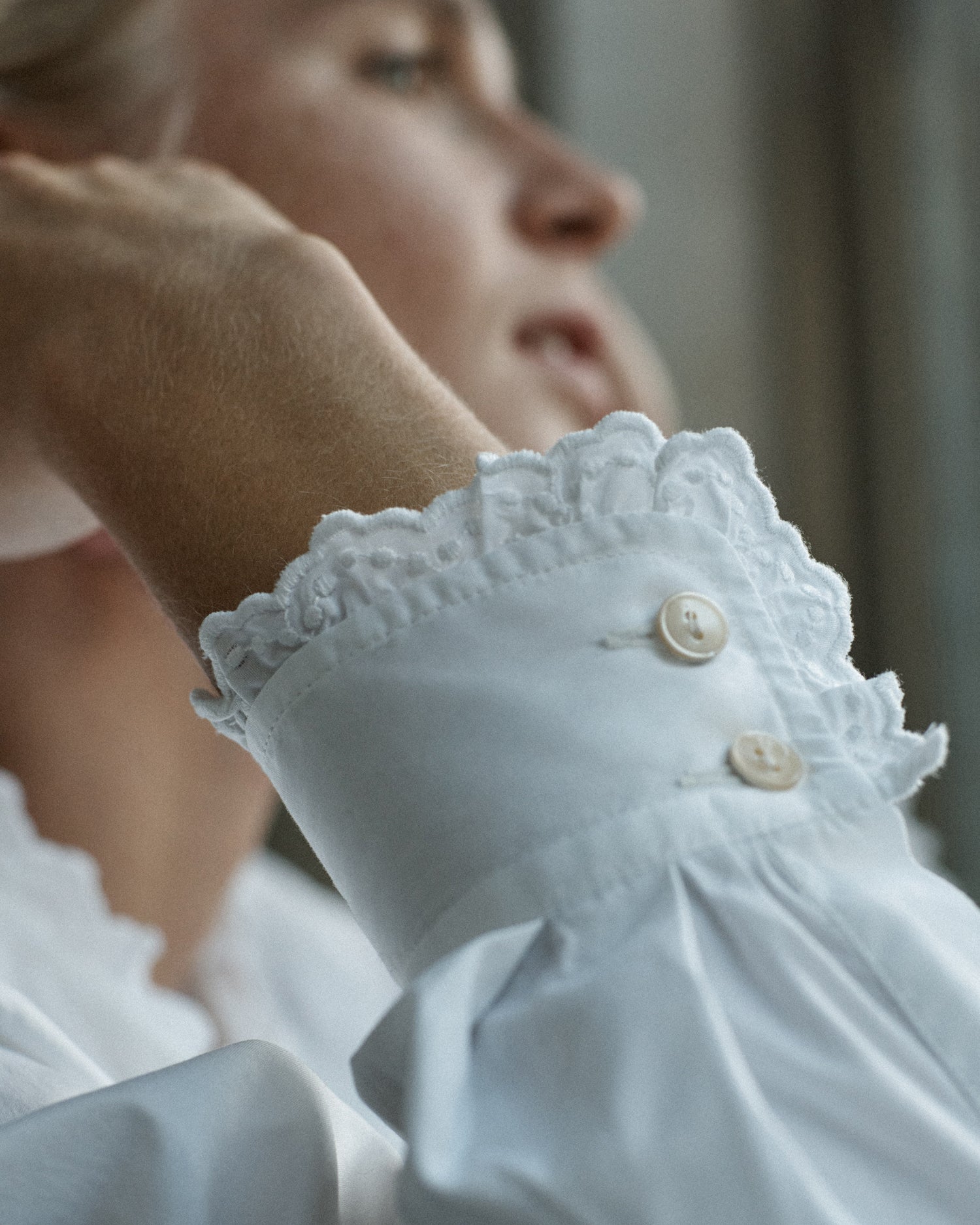 Close-up of a woman's wrist. She is wearing a long sleeve white cotton blouse with eyelet trim at the cuff.