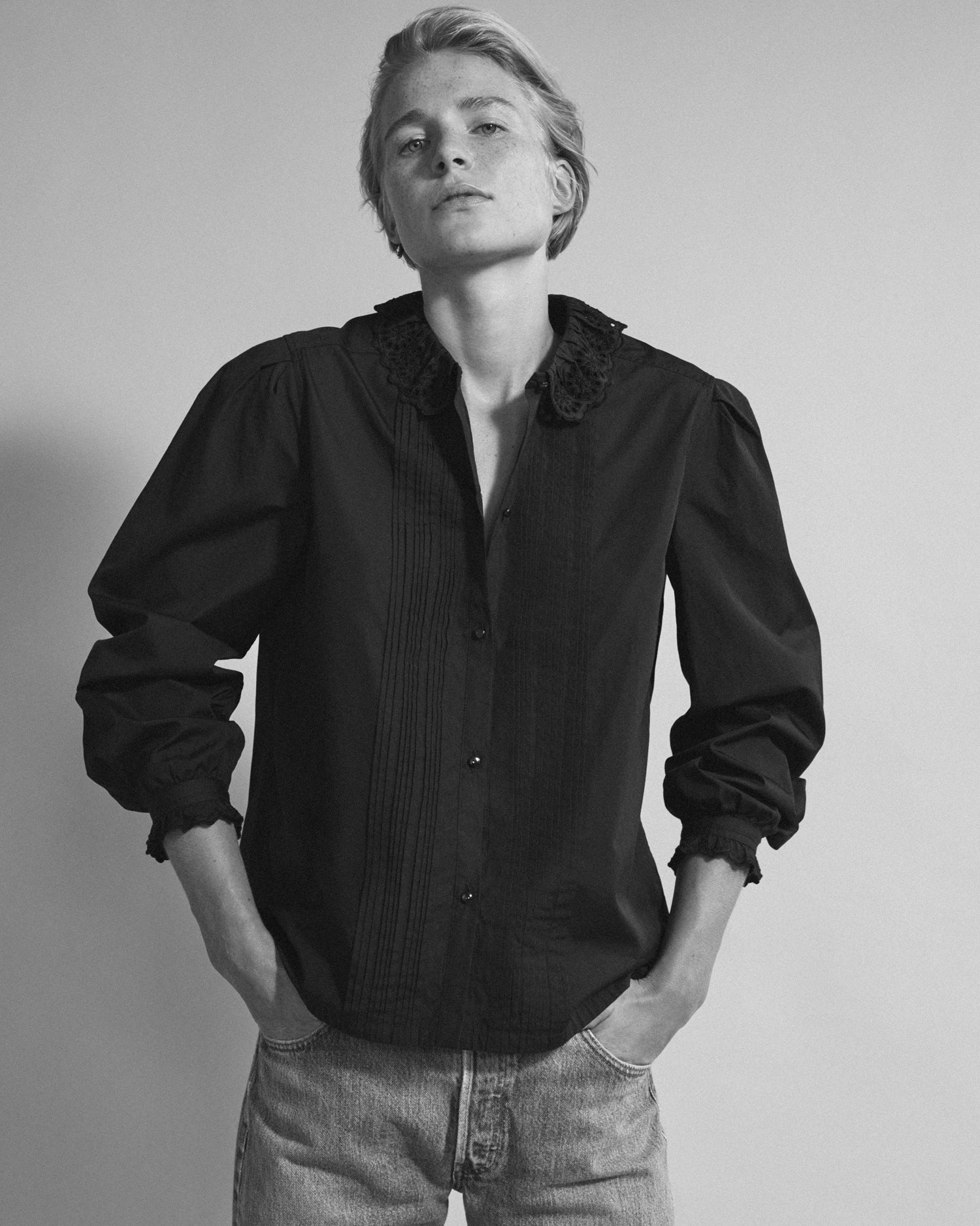 Woman standing with hands in her pockets wearing a long sleeve button-down blouse and jeans. Blouse is black cotton.