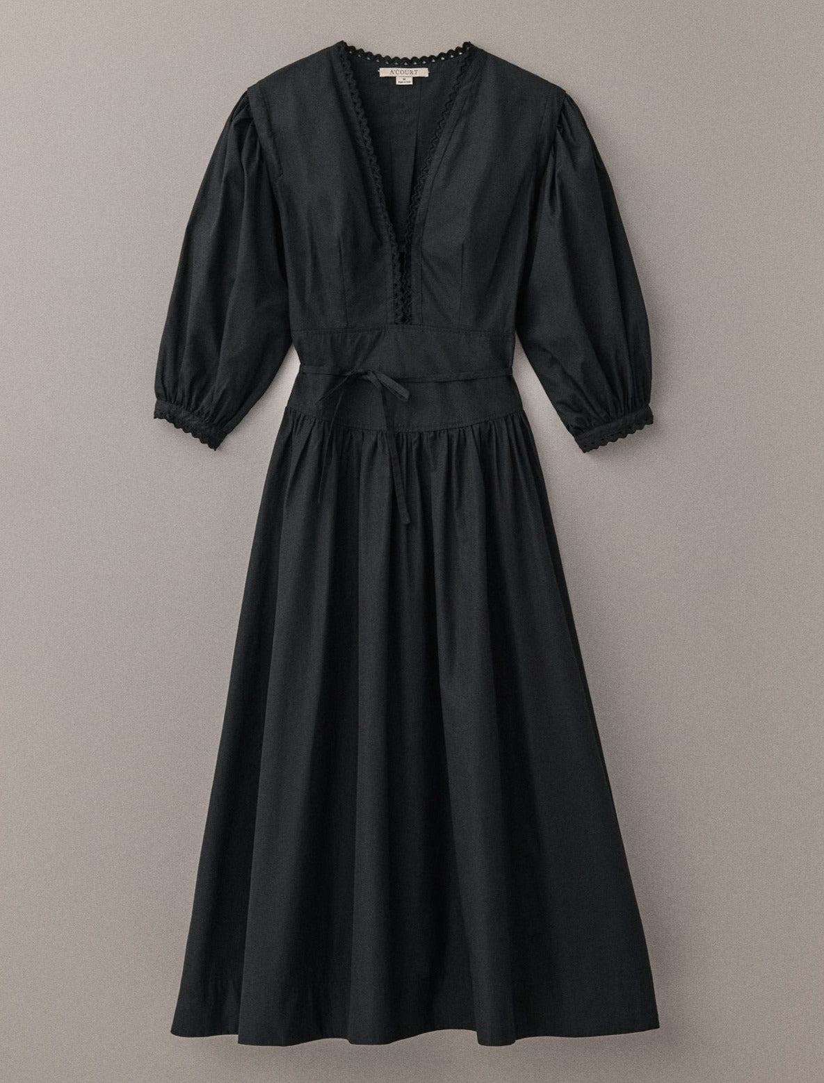 A black cotton long-sleeve maxi dress with puff sleeves and eyelet trim lies flat on a light brown field.