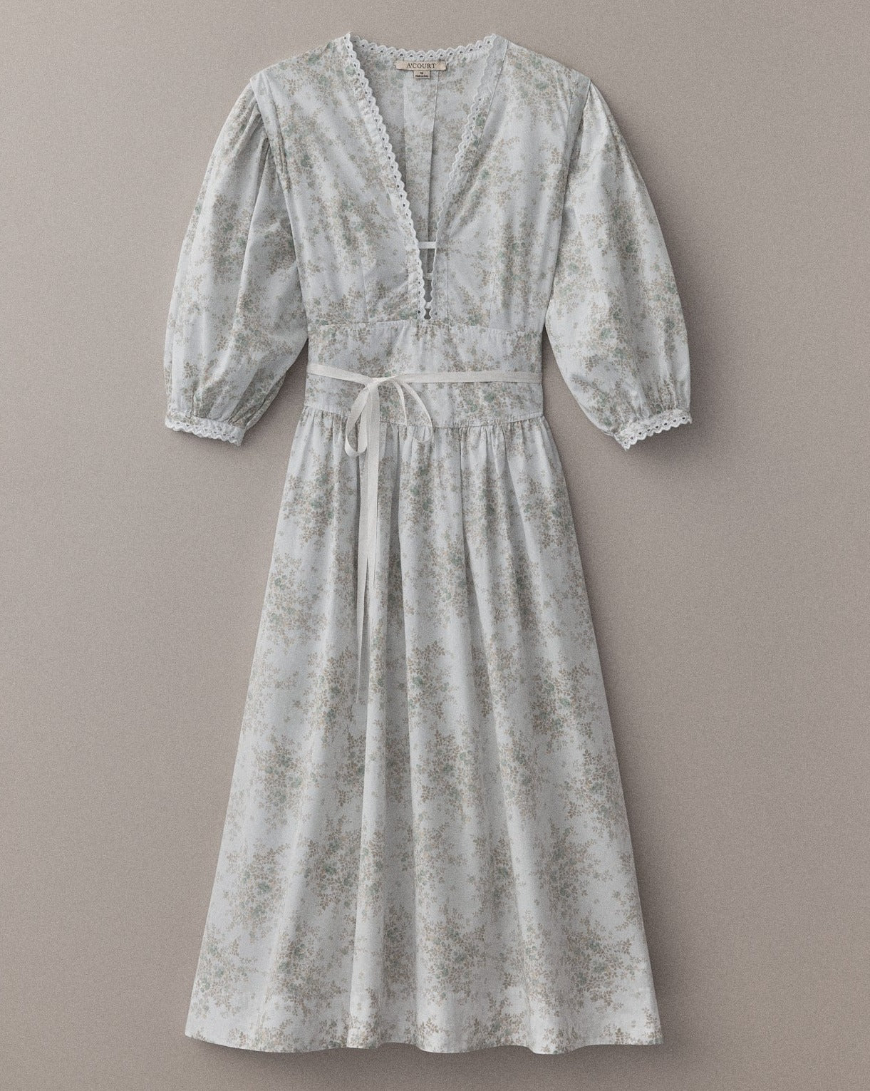 A white and blue floral long-sleeve maxi dress with puff sleeves and eyelet trim lies flat on a light brown field.