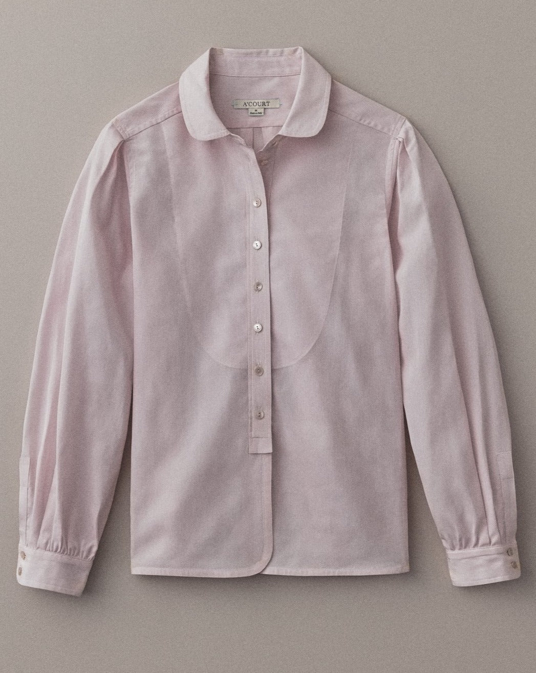 A long sleeve blouse in dusty rose cotton with a classic menswear silhouette lies flat on a light brown field.