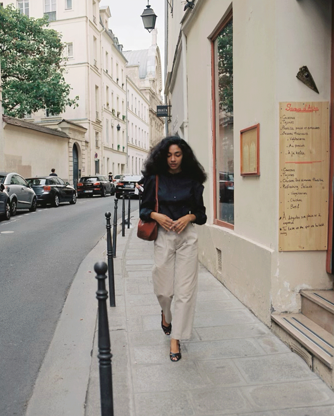 A GIF of different shots of a brunette woman walking the streets of Paris in a series of black cotton blouses and dresses.