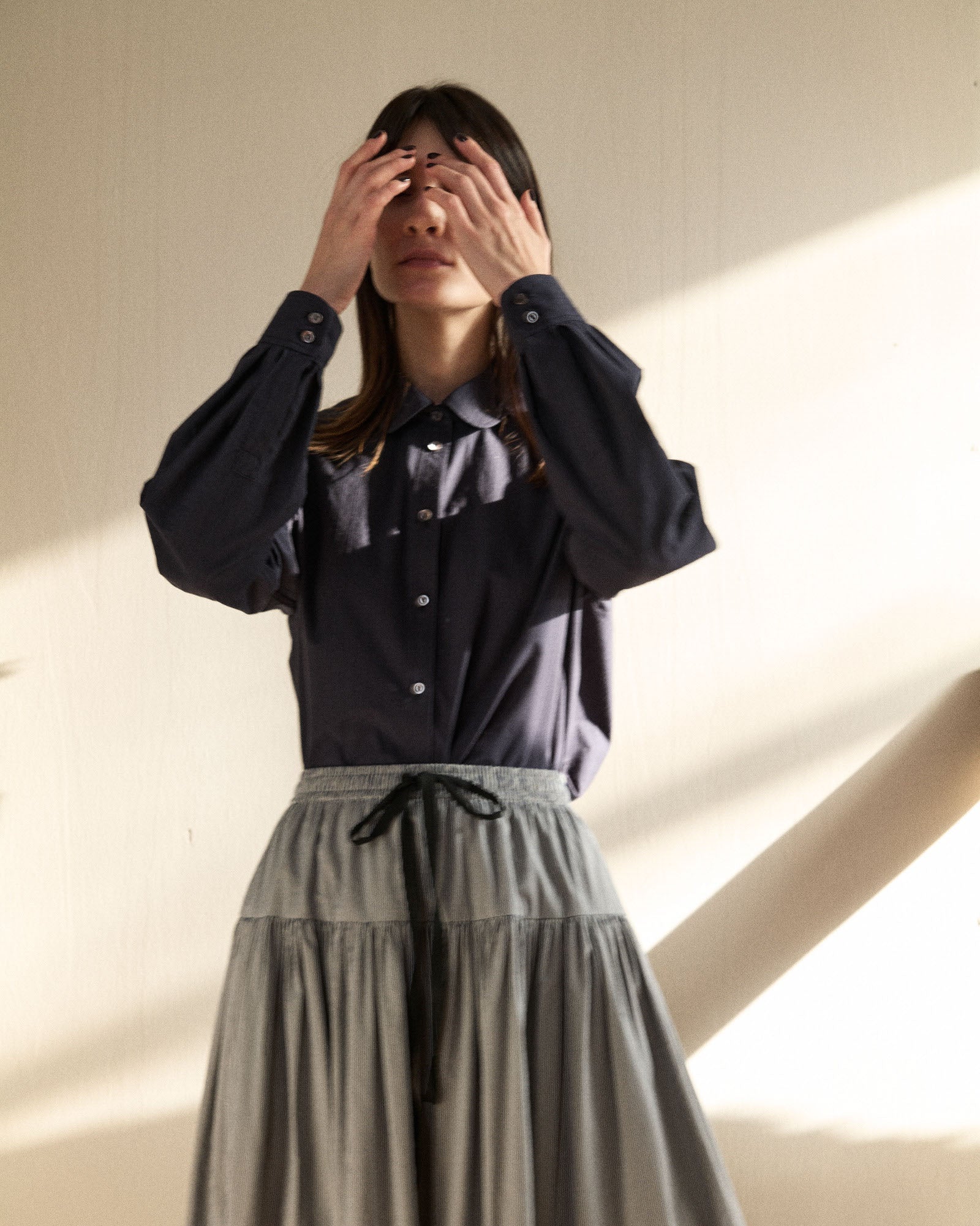 Person wearing a navy blouse and gray skirt against a neutral background