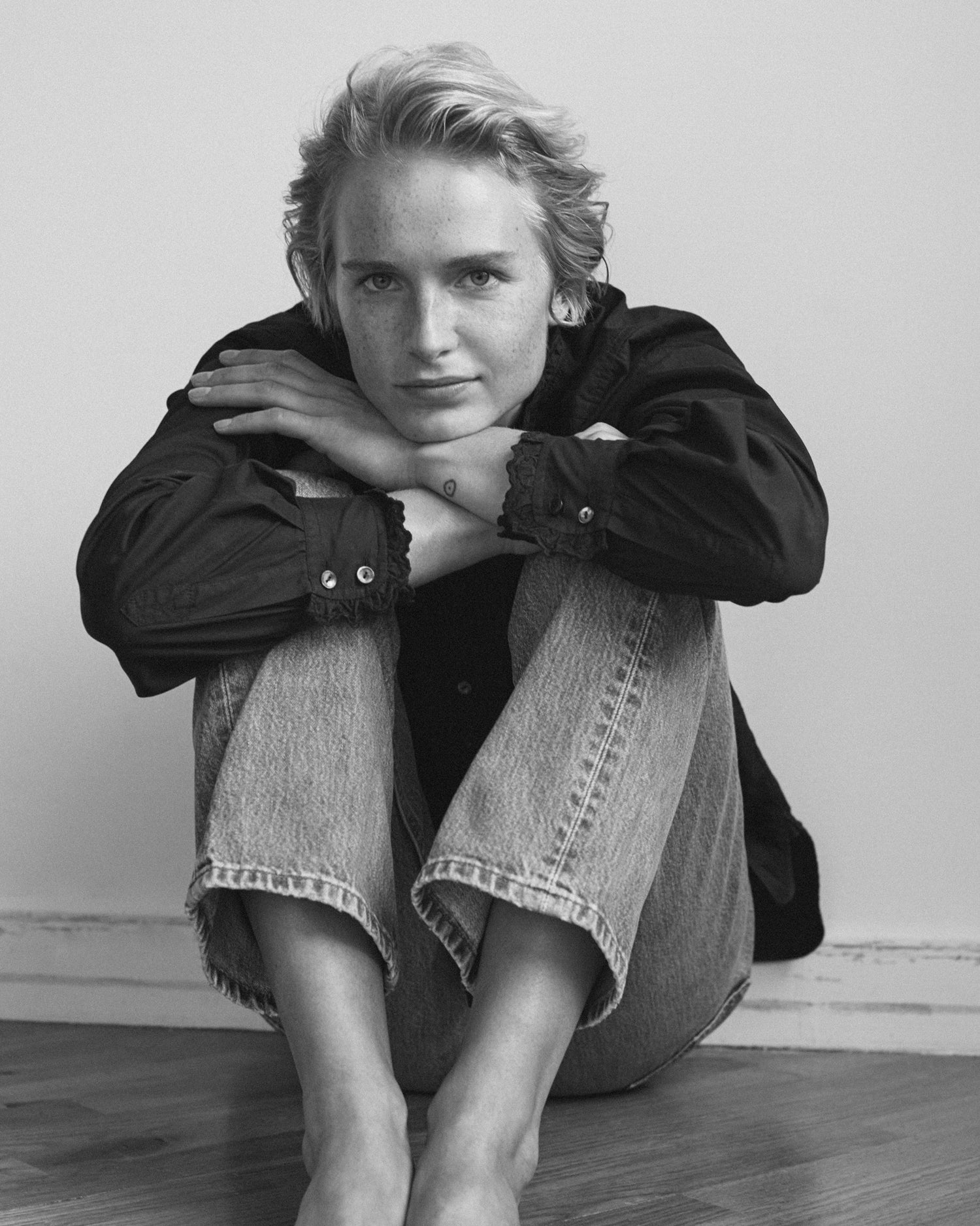Woman sitting on the ground with her arms and head on her knees. She is wearing a long sleeve black blouse and jeans.