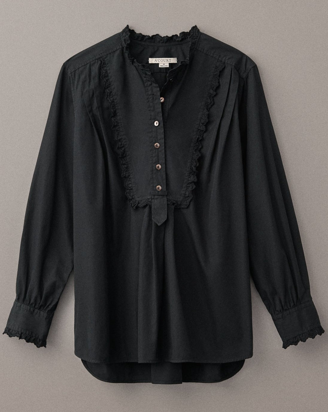 A black cotton blouse with a tuxedo-style bib, eyelet trim and half button closure lies flat on a light brown field.