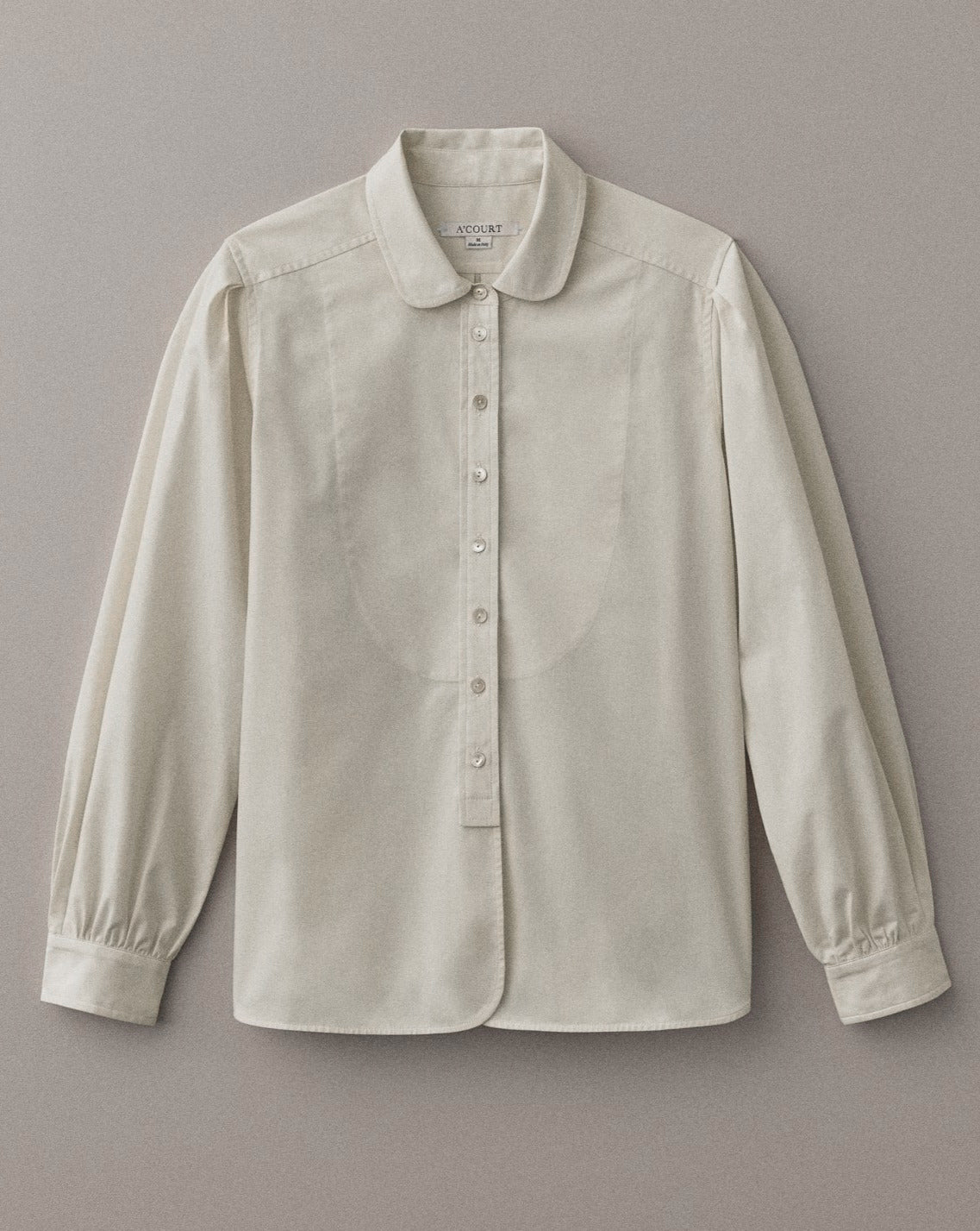 A long sleeve buttery cream button down with a classic menswear silhouette lies on a light brown field.