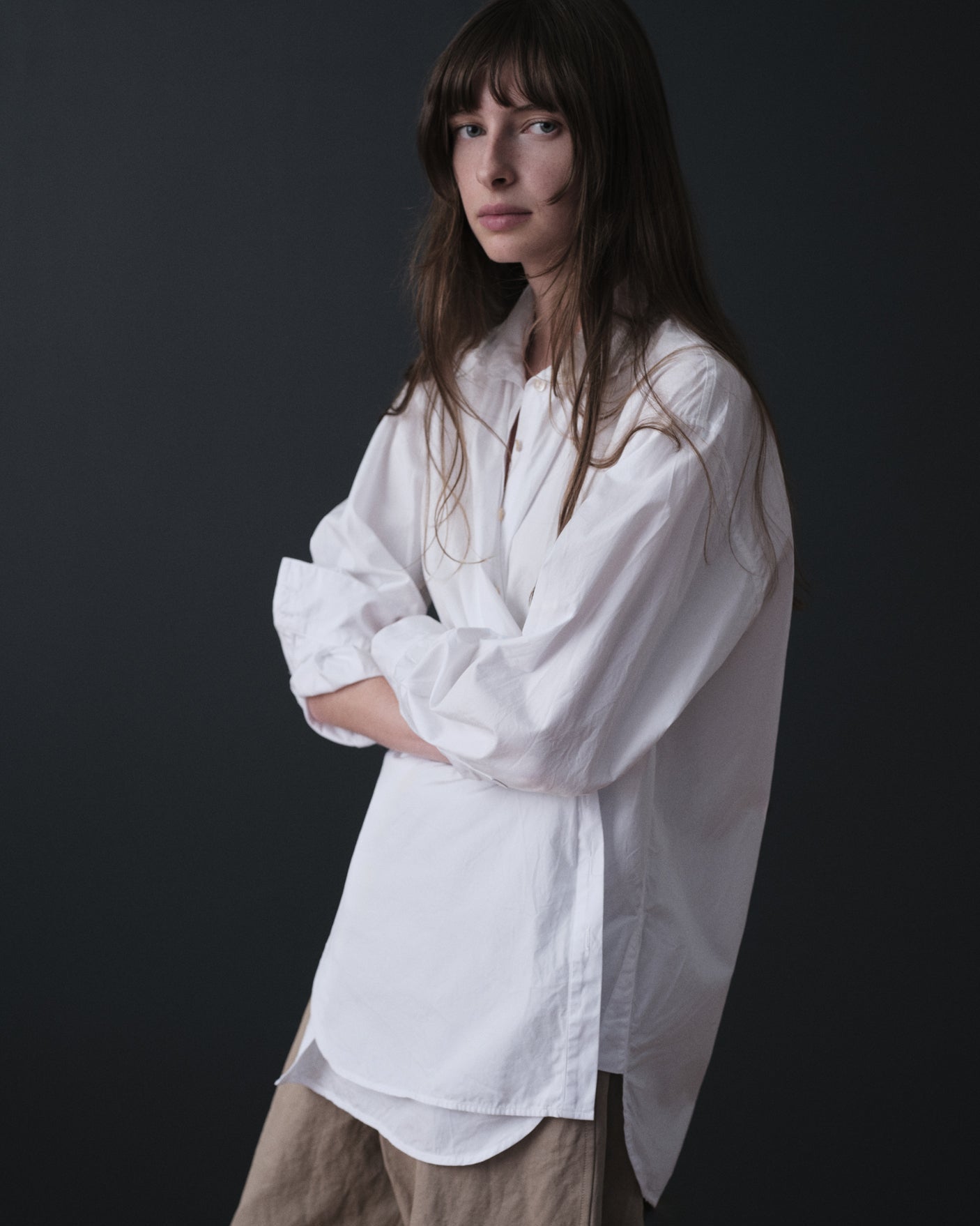 Woman wearing a white shirt and beige pants against a black background