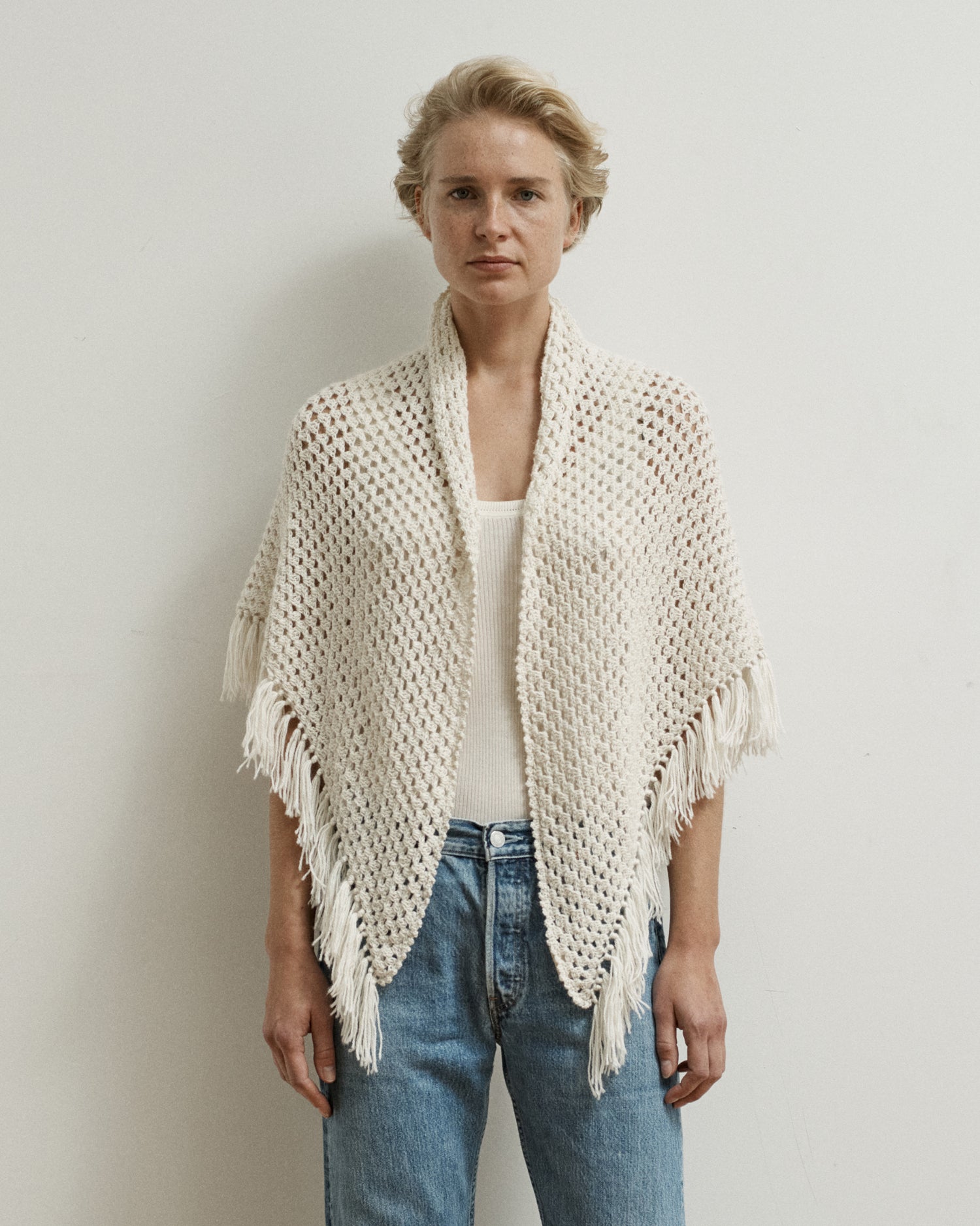 Woman standing with a cream-colored shawl draped over her shoulders. Shawl is hand-crocheted and has fringe.