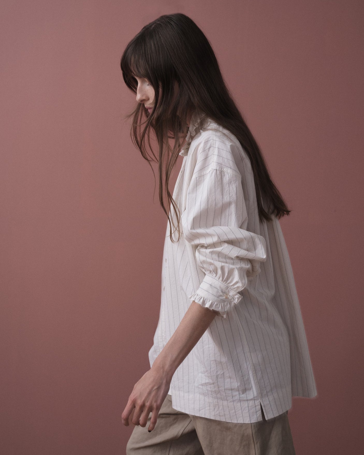 Woman wearing a white blouse with ruffled sleeves against a pink background