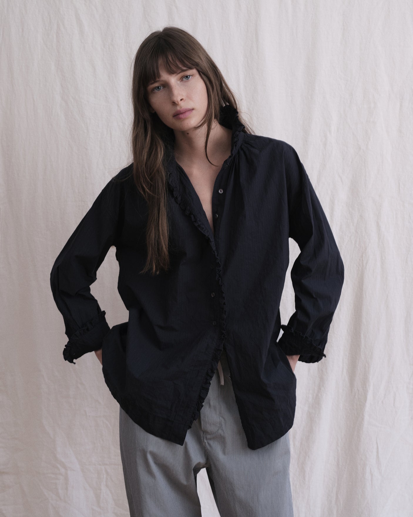Woman wearing a navy shirt and light gray pants against a white background