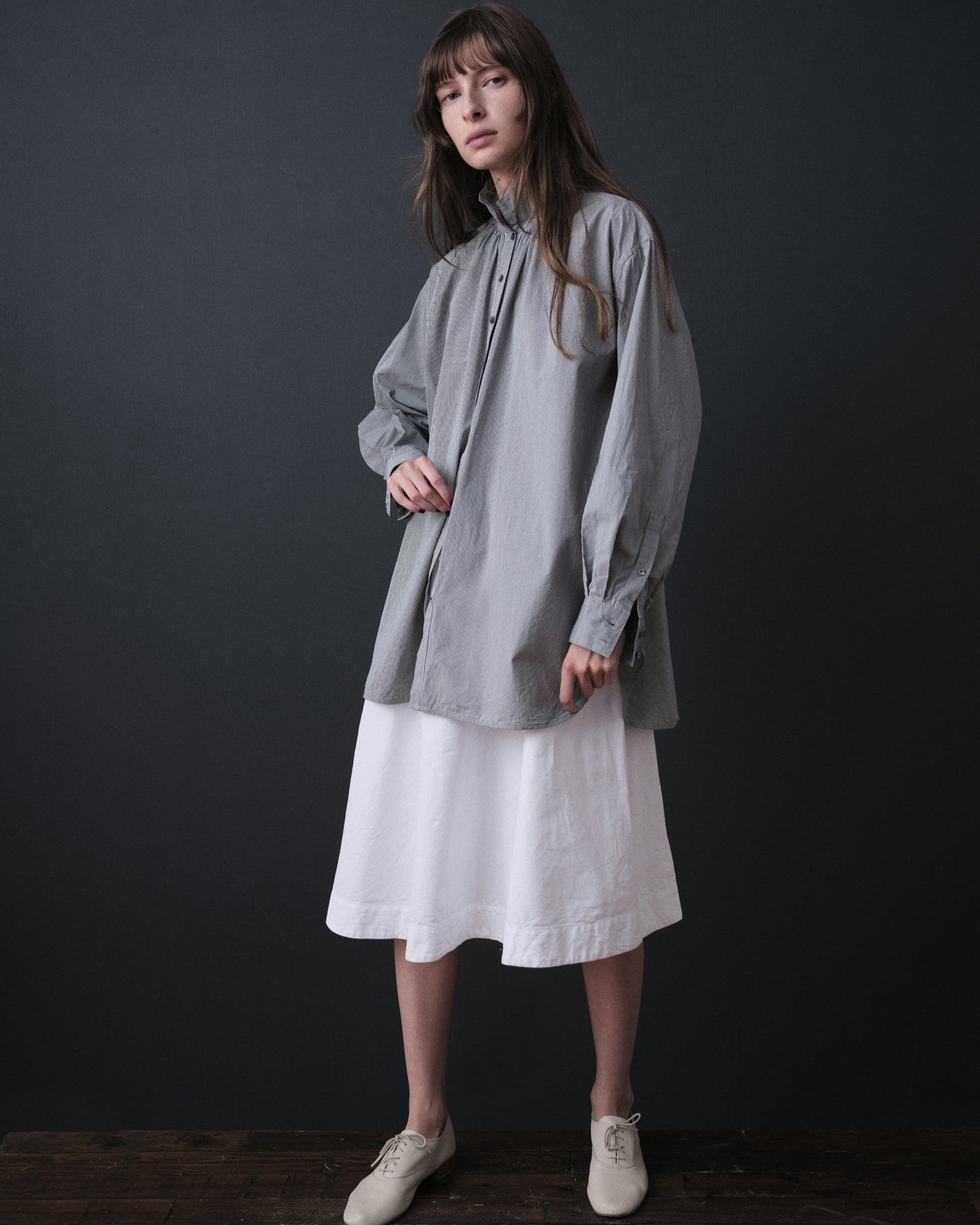 Woman wearing a gray shirt over a white dress against a dark background
