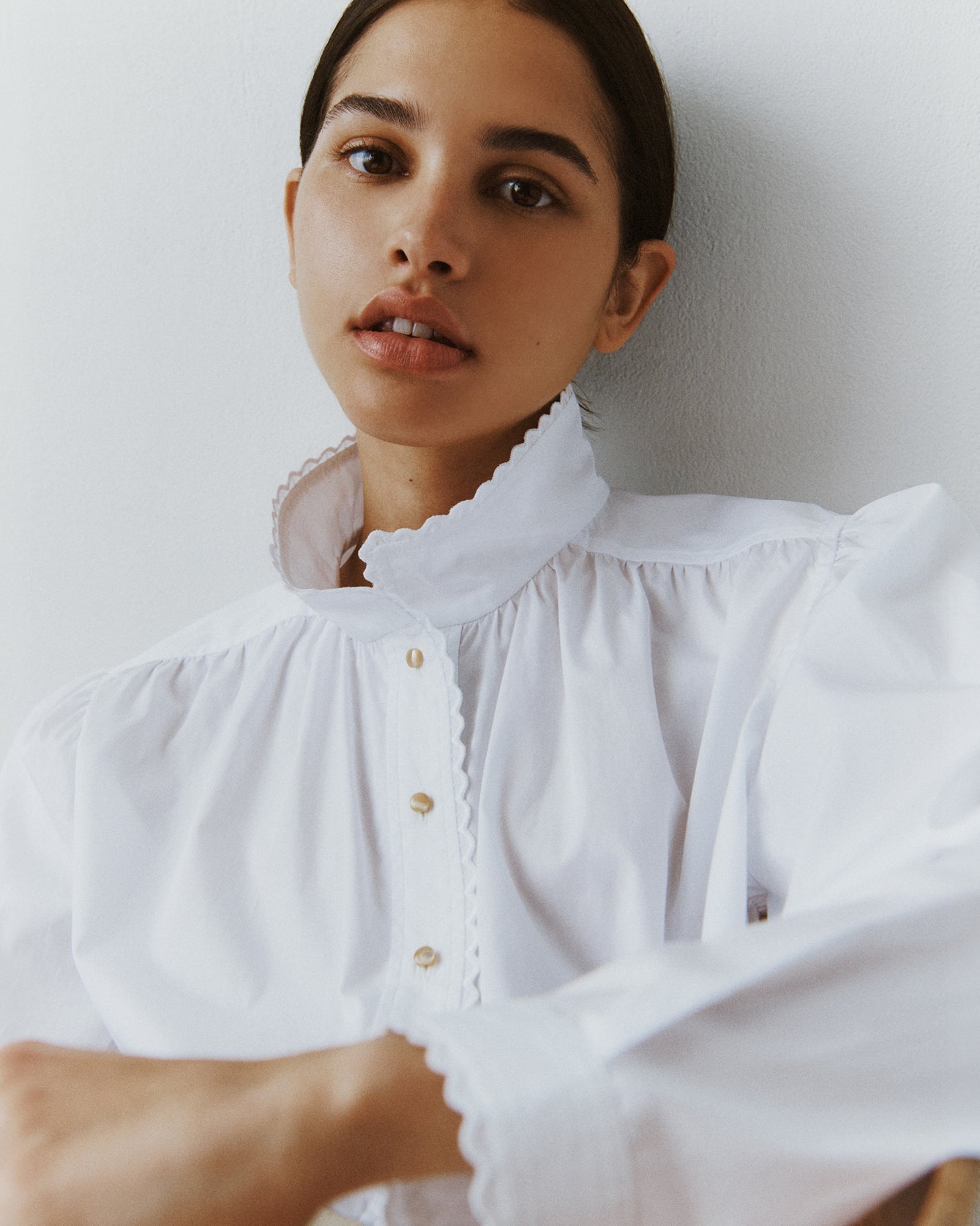 Close-up of a brunette woman wearing a white cotton blouse with eyelet trim at the collar and cuffs.