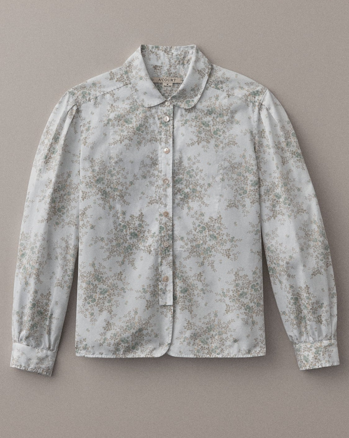 A long sleeve blouse in floral cotton with a classic menswear silhouette lies flat on a light brown field.