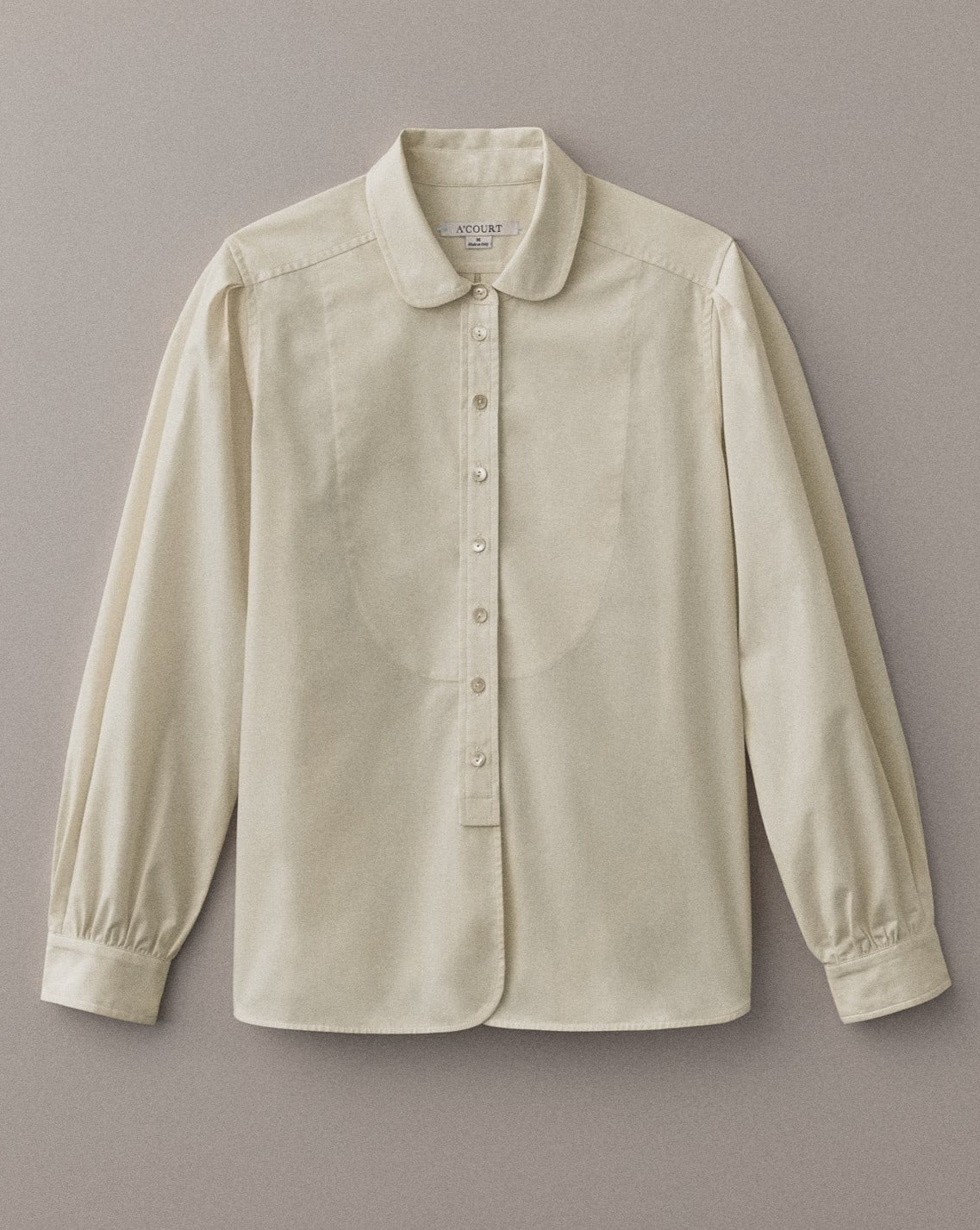 A long sleeve buttery cream button down with a classic menswear silhouette lies on a light brown field.