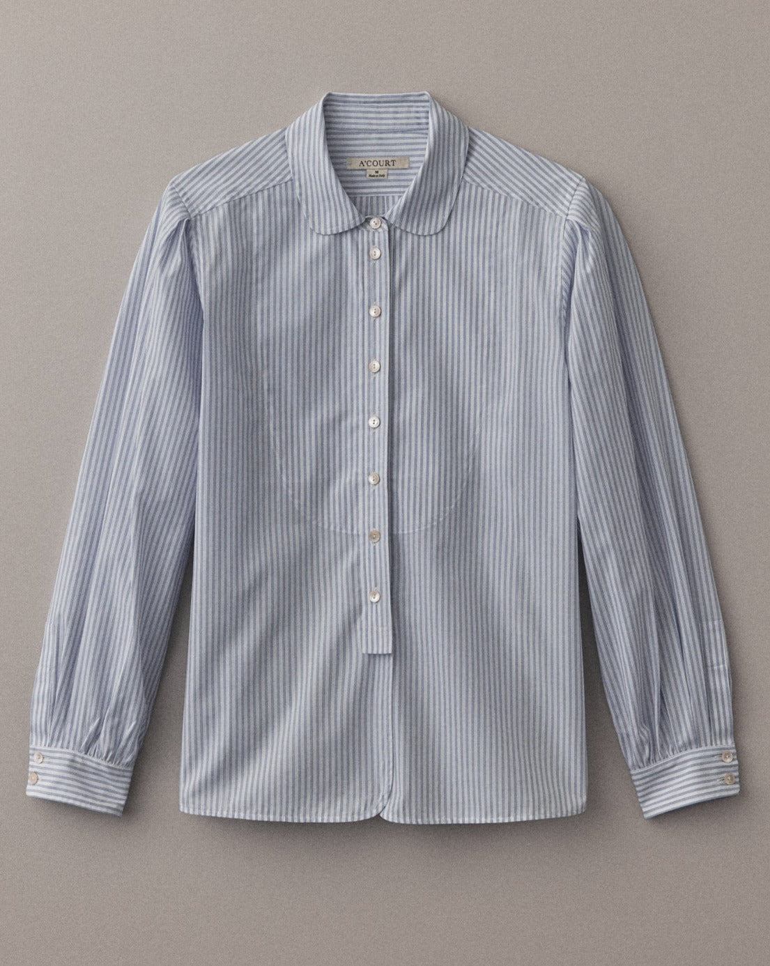 A long sleeve white striped button down with a classic menswear silhouette lies on a light brown field.
