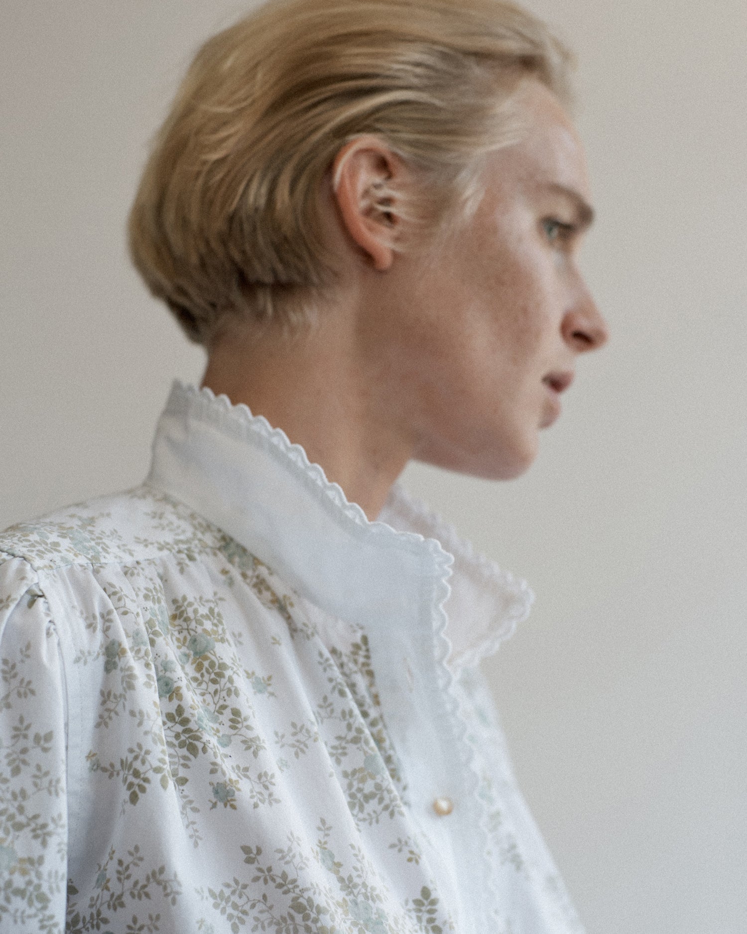 Portrait of a woman's face looking away from camera. She is wearing a floral cotton blouse with eyelet collar trim.
