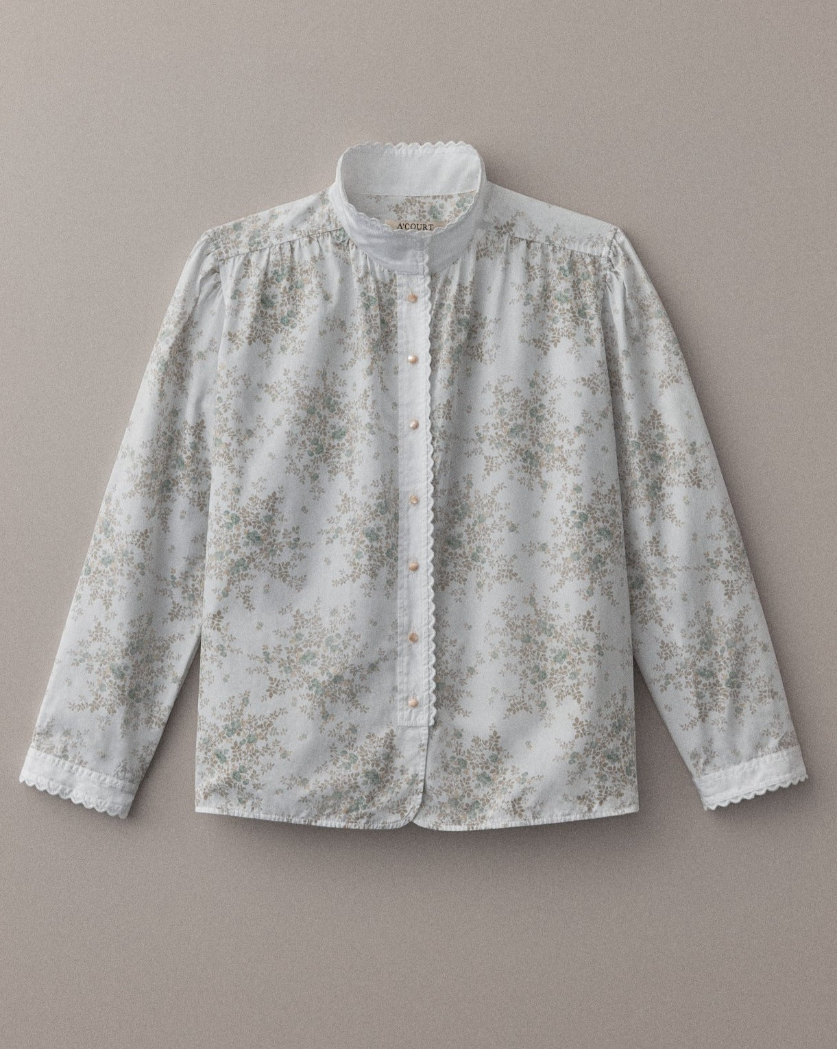 A long sleeve blouse in floral cotton with eyelet trim at the collar and cuffs lies flat on a light brown field.